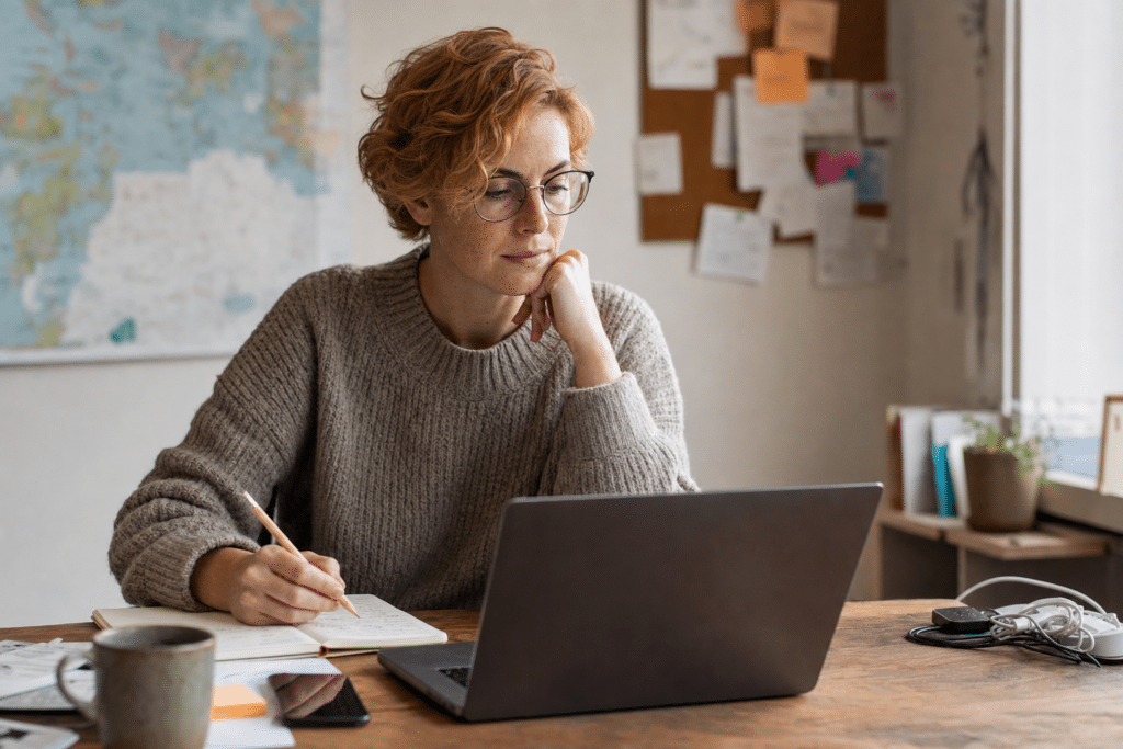 Domain befektető jegyzetel íróasztalnál, laptop mellett — domain név type-in forgalom