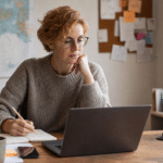 Domain befektető jegyzetel íróasztalnál, laptop mellett — domain név type-in forgalom