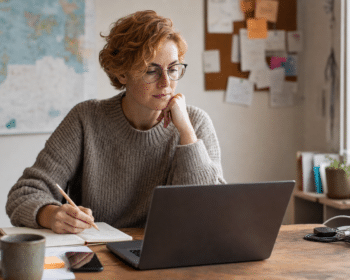 Domain befektető jegyzetel íróasztalnál, laptop mellett — domain név type-in forgalom